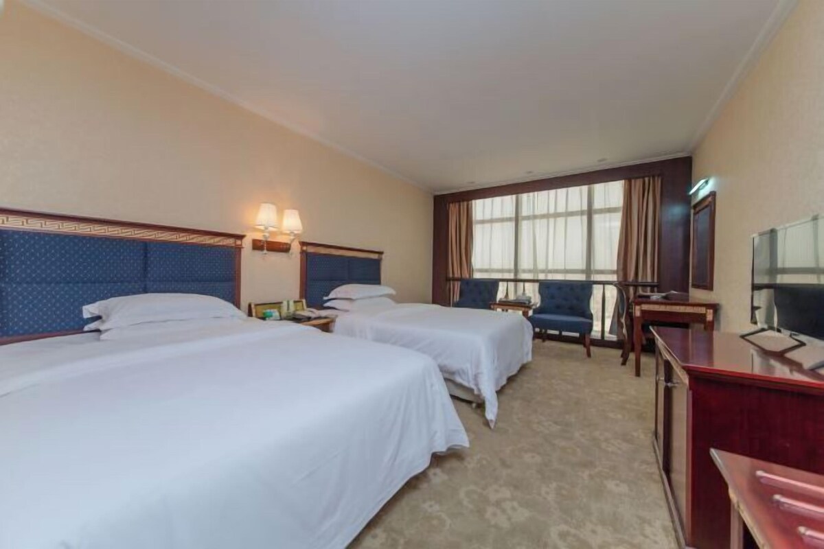 Habitación de hotel con dos camas, un escritorio, una silla, un televisor y una ventana con cortinas.