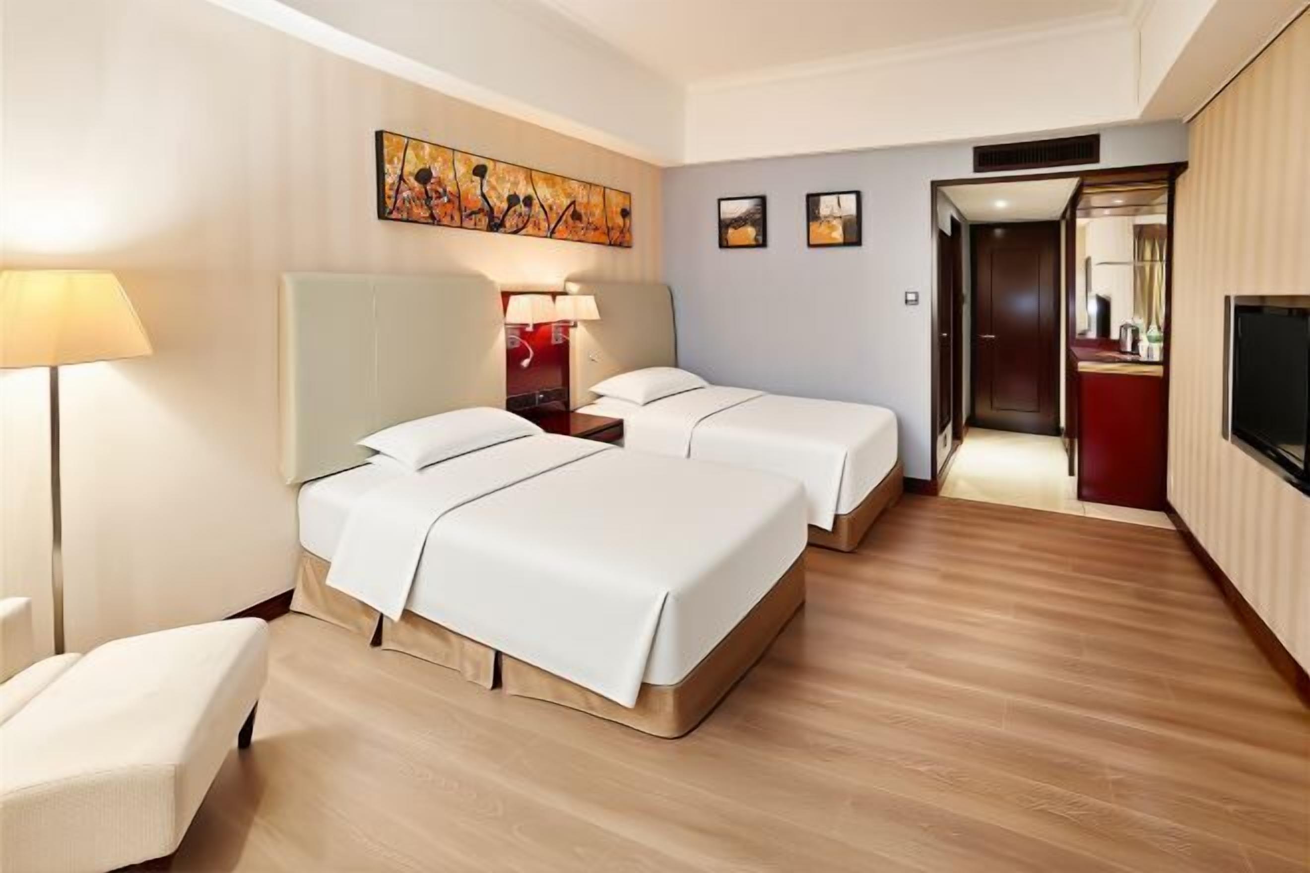 Habitación de hotel con dos camas, un escritorio, una silla, un televisor y un cuadro en la pared.