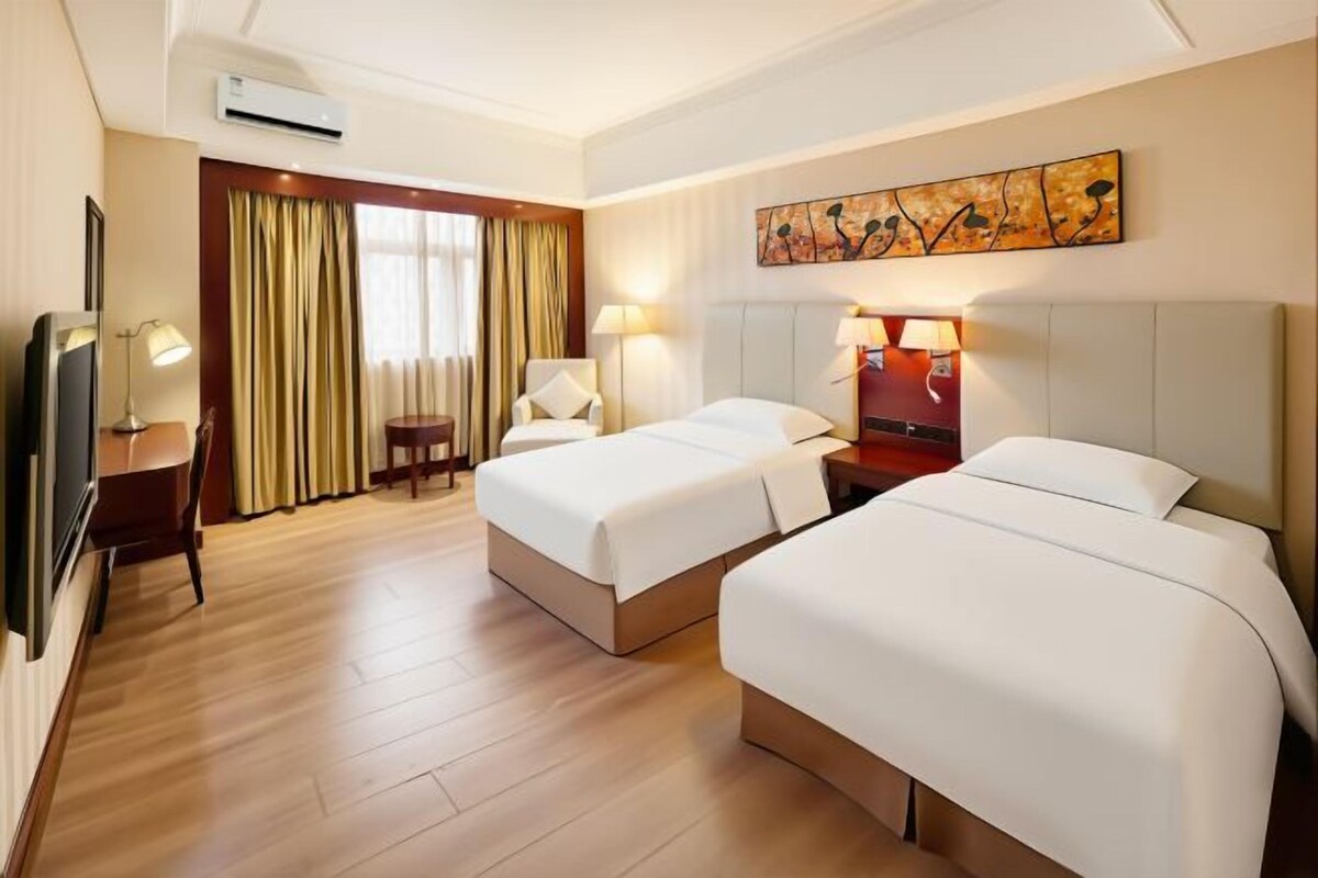 A hotel room with two beds, a desk, a TV, a chair, and a painting on the wall.