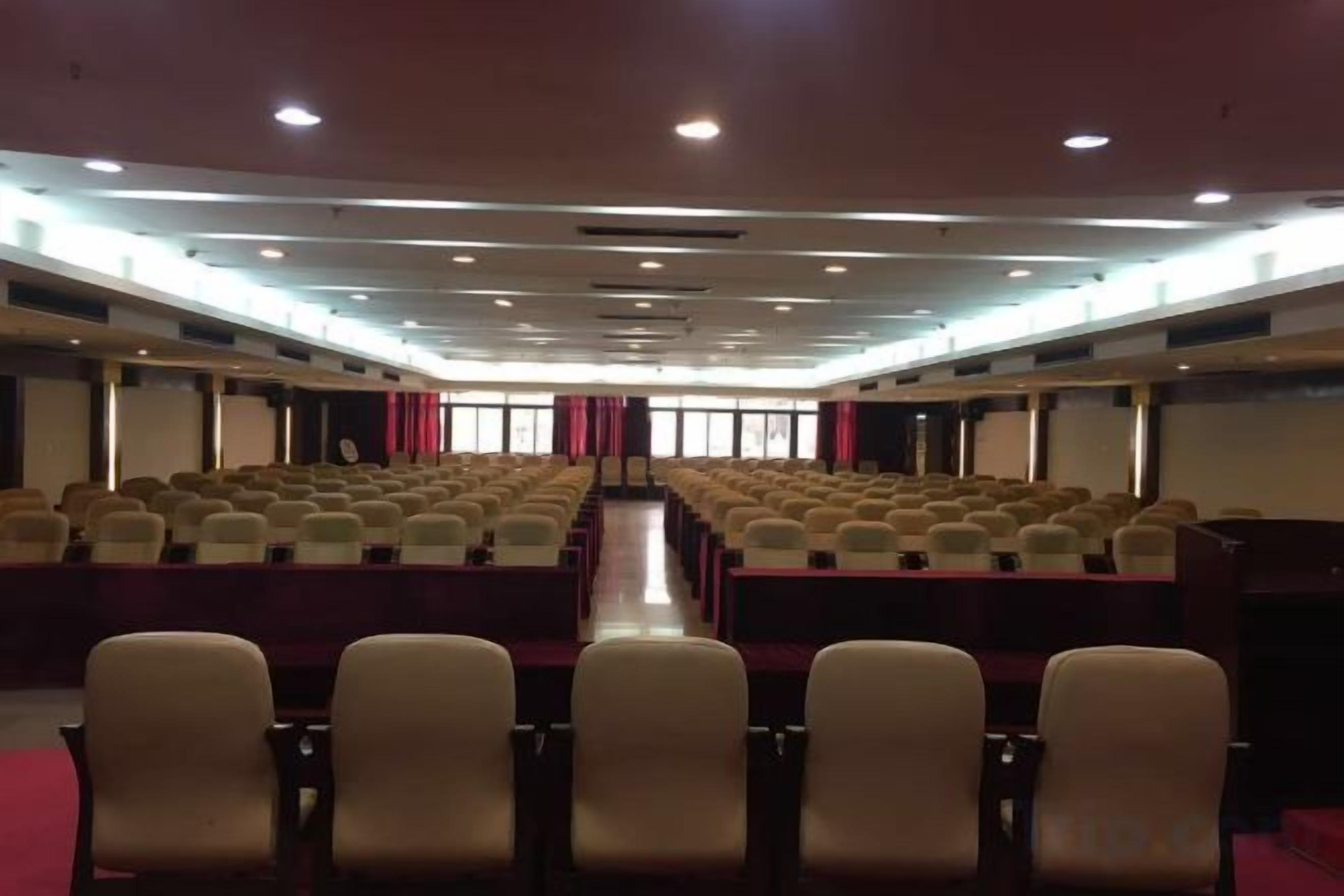 A conference room with rows of chairs, a stage, and a projector screen.