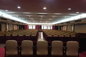 Un salón de conferencias con filas de sillas, un escenario y una pantalla de proyector.