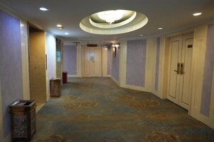 Un pasillo de hotel con alfombra estampada, puertas y una lámpara de techo circular.