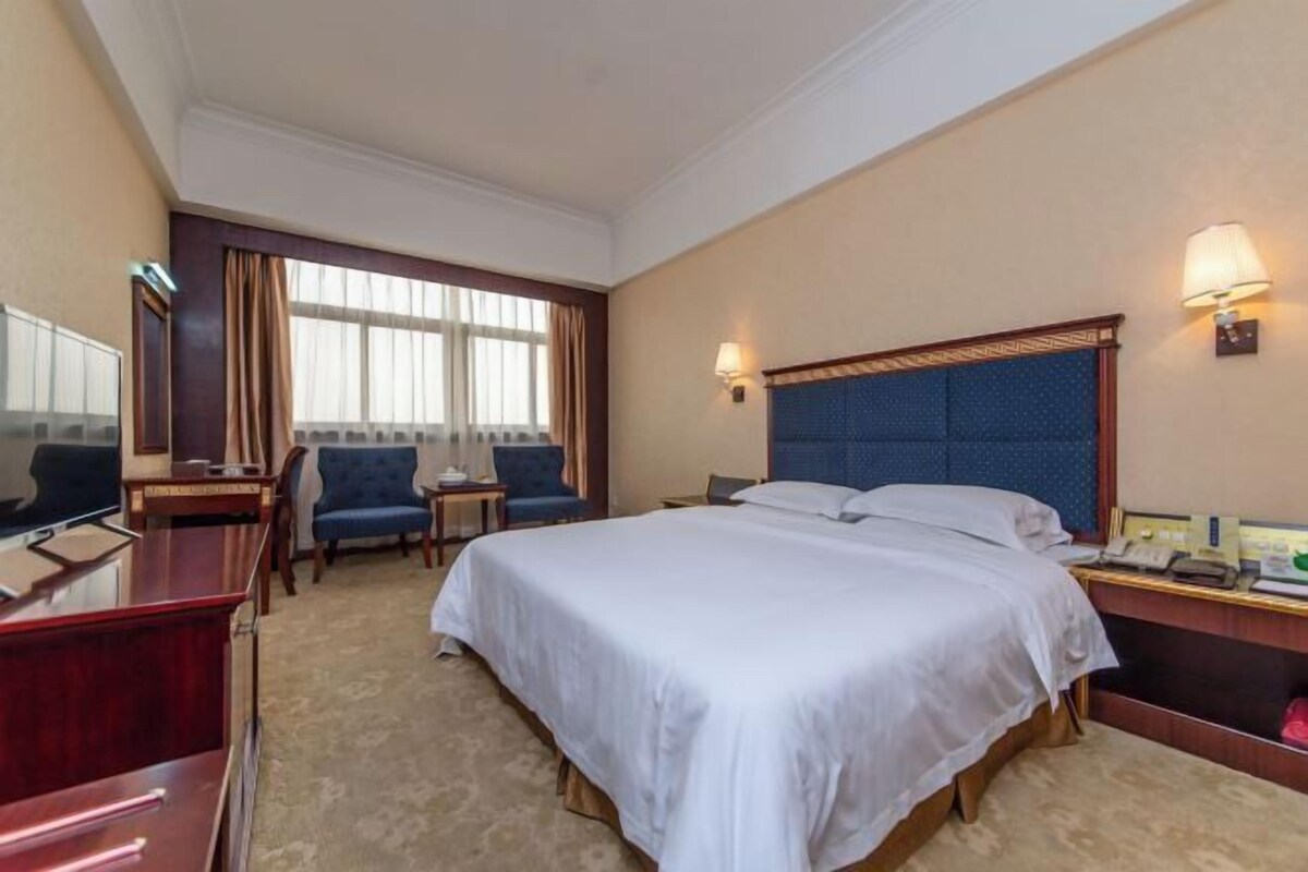 Una habitación de hotel con cama, escritorio, silla, televisor y ventana.