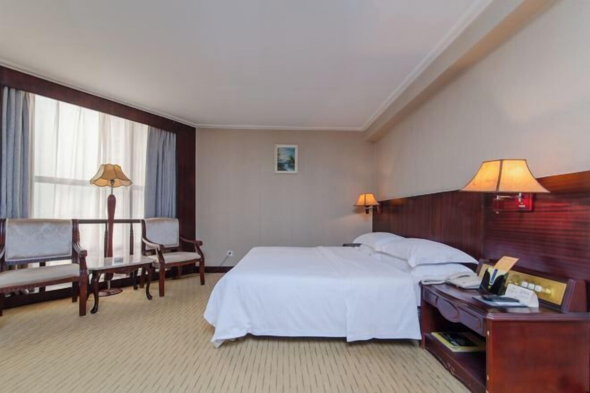 Una habitación de hotel con una cama, dos sillas, un escritorio y una lámpara.