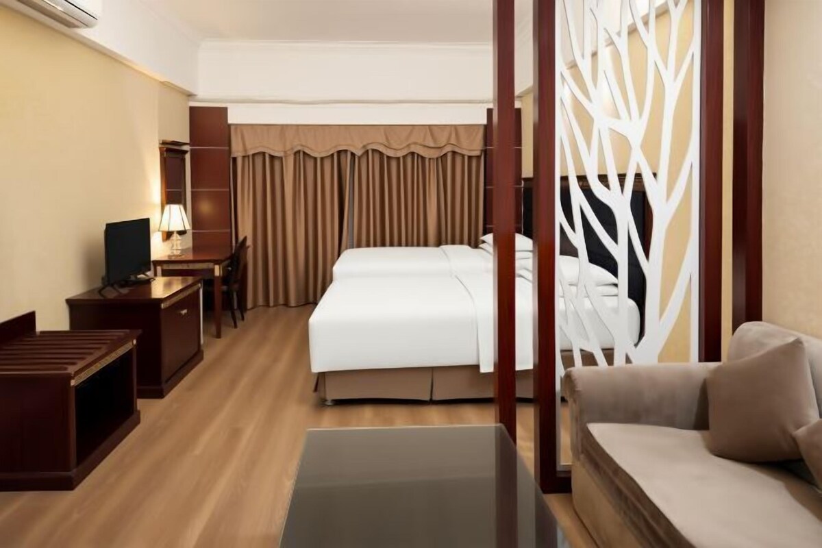 A hotel room with a bed, a desk with a lamp, a chair, a sofa, and a decorative screen.