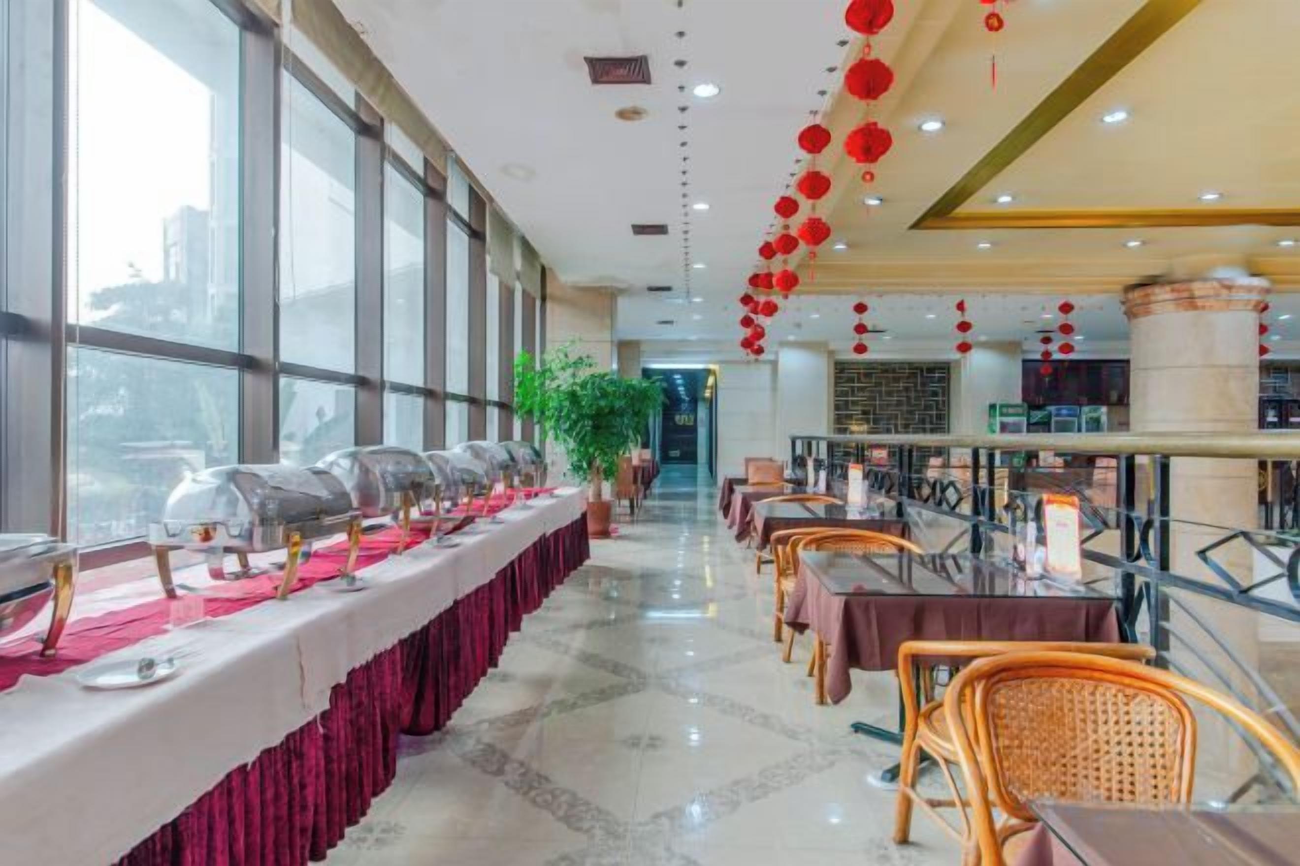 Un comedor de hotel con una larga mesa dispuesta para un banquete, rodeada de sillas, y grandes ventanales en un lateral.