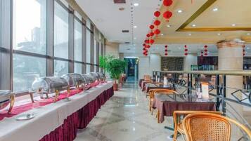 Un comedor de hotel con una larga mesa dispuesta para un banquete, rodeada de sillas, y grandes ventanales en un lateral.