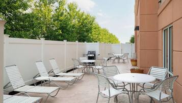 An outdoor patio with metal chairs and tables, a barbecue grill, and a white fence.