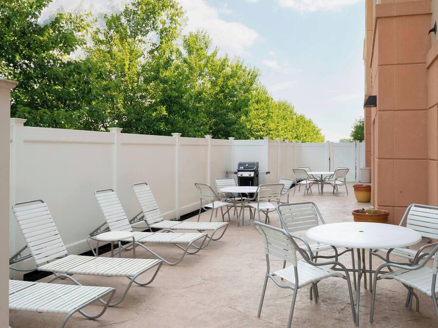 An outdoor patio with metal chairs and tables, a barbecue grill, and a white fence.