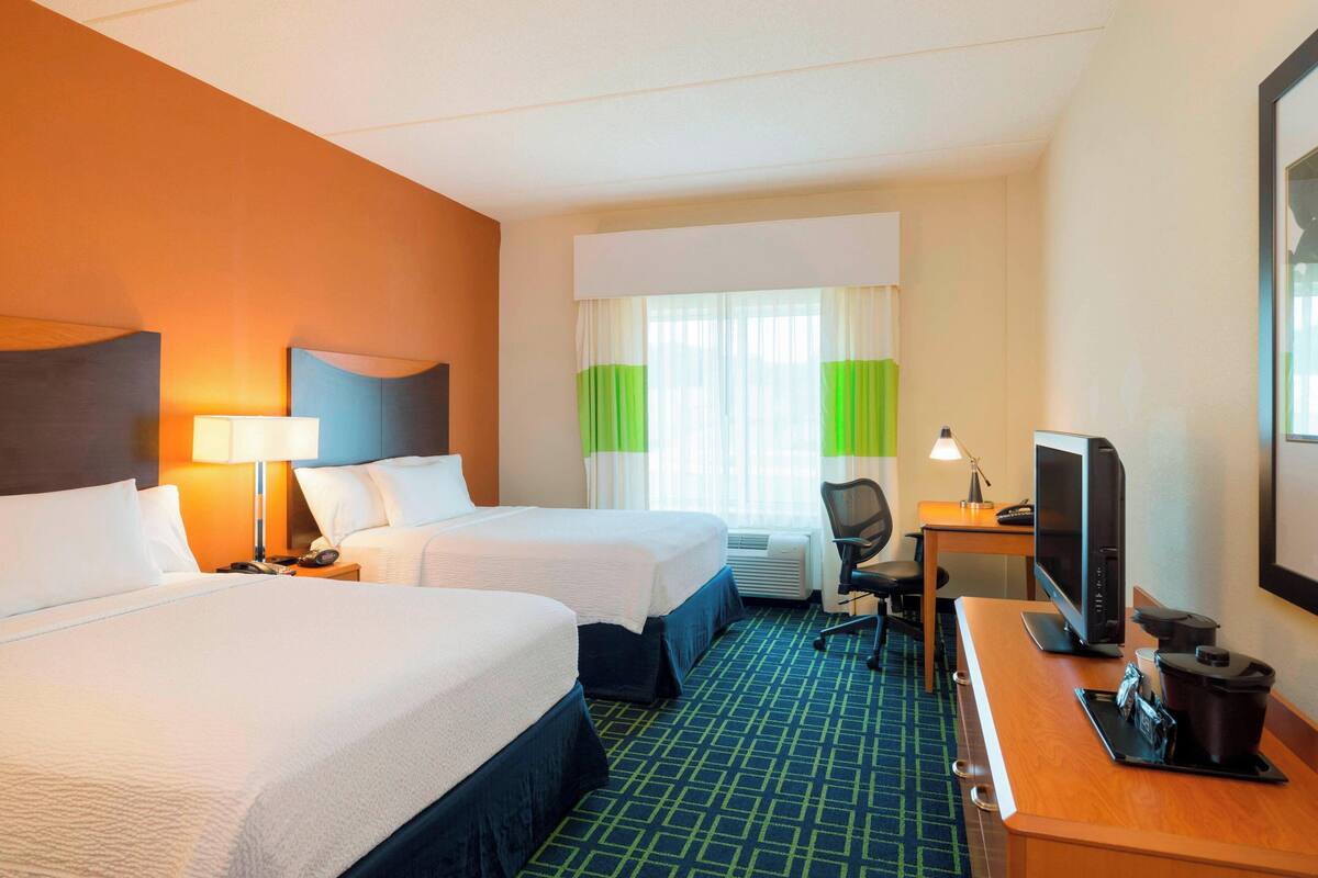A hotel room with two beds, a desk with a computer, and a television.