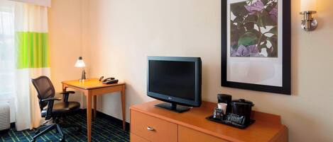 A hotel room with a desk, chair, television, and a framed floral artwork on the wall.