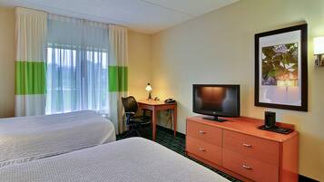 A hotel room with two beds, a desk with a chair, a television, a dresser, and a framed picture on the wall.