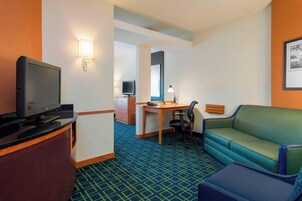 A hotel room with a television, desk, chair, sofa, and a large mirror.