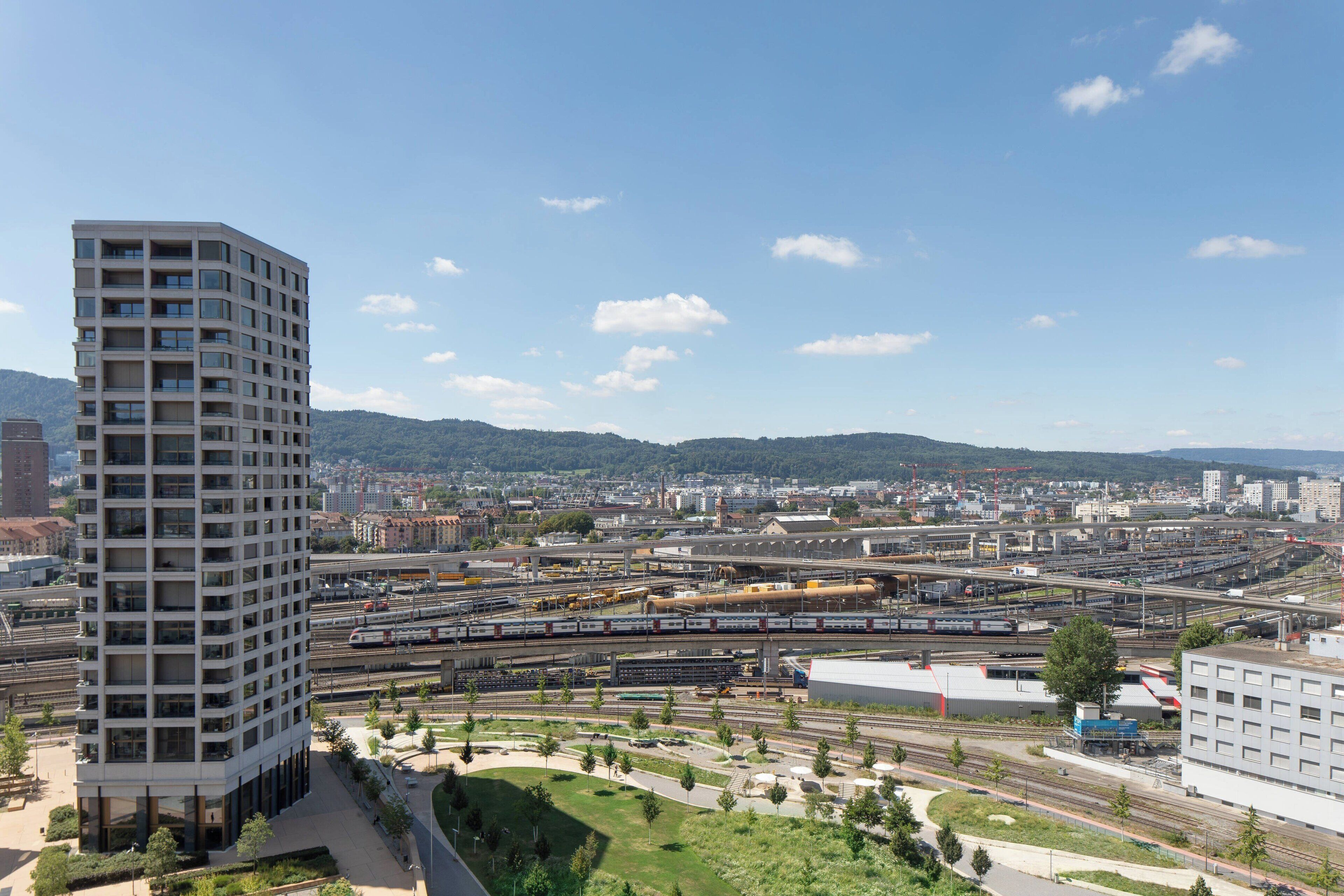 A modern high-rise building with a clear view of a complex railway system in the background.