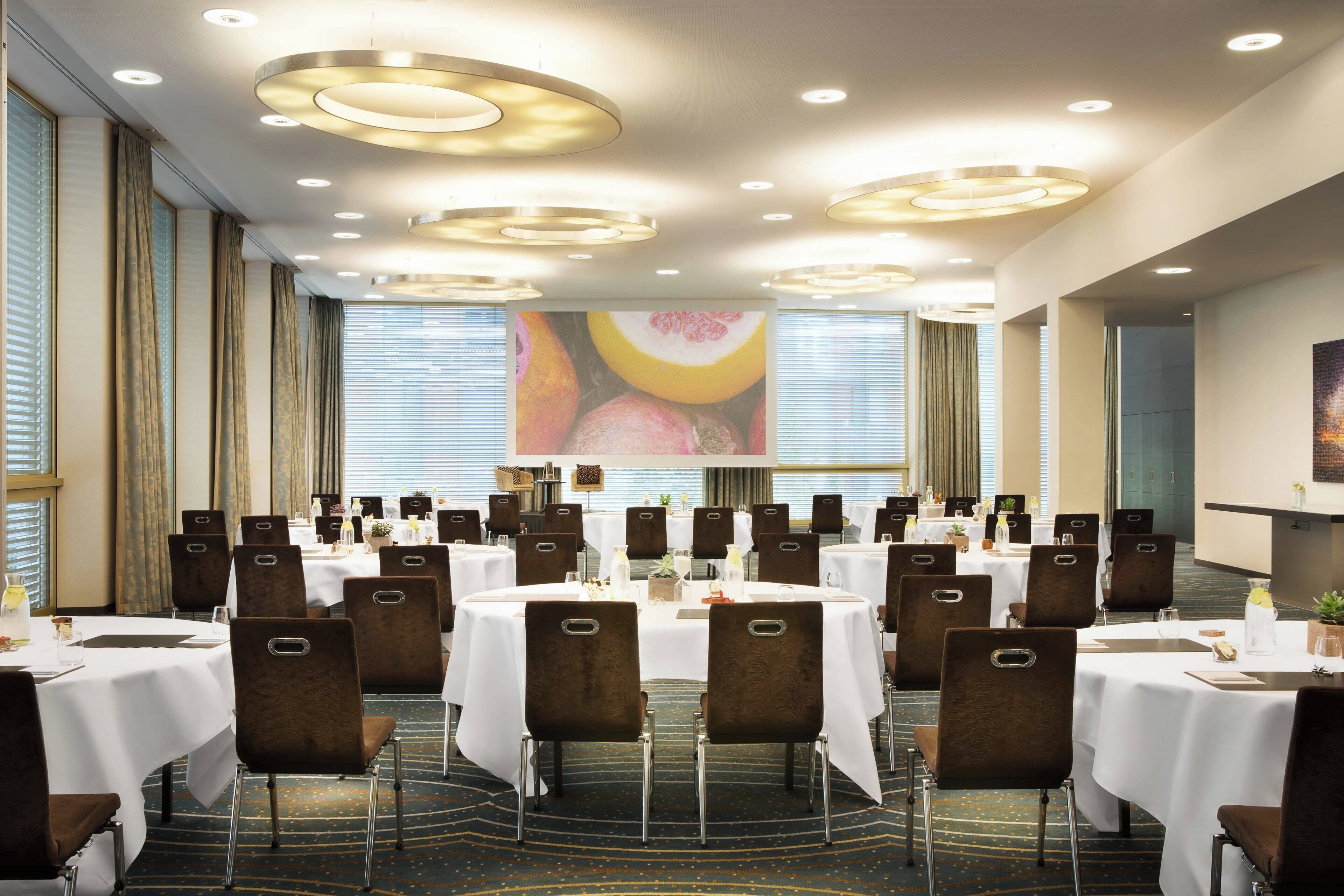 Une salle de conférence avec des tables rondes, des chaises marron et des nappes blanches.