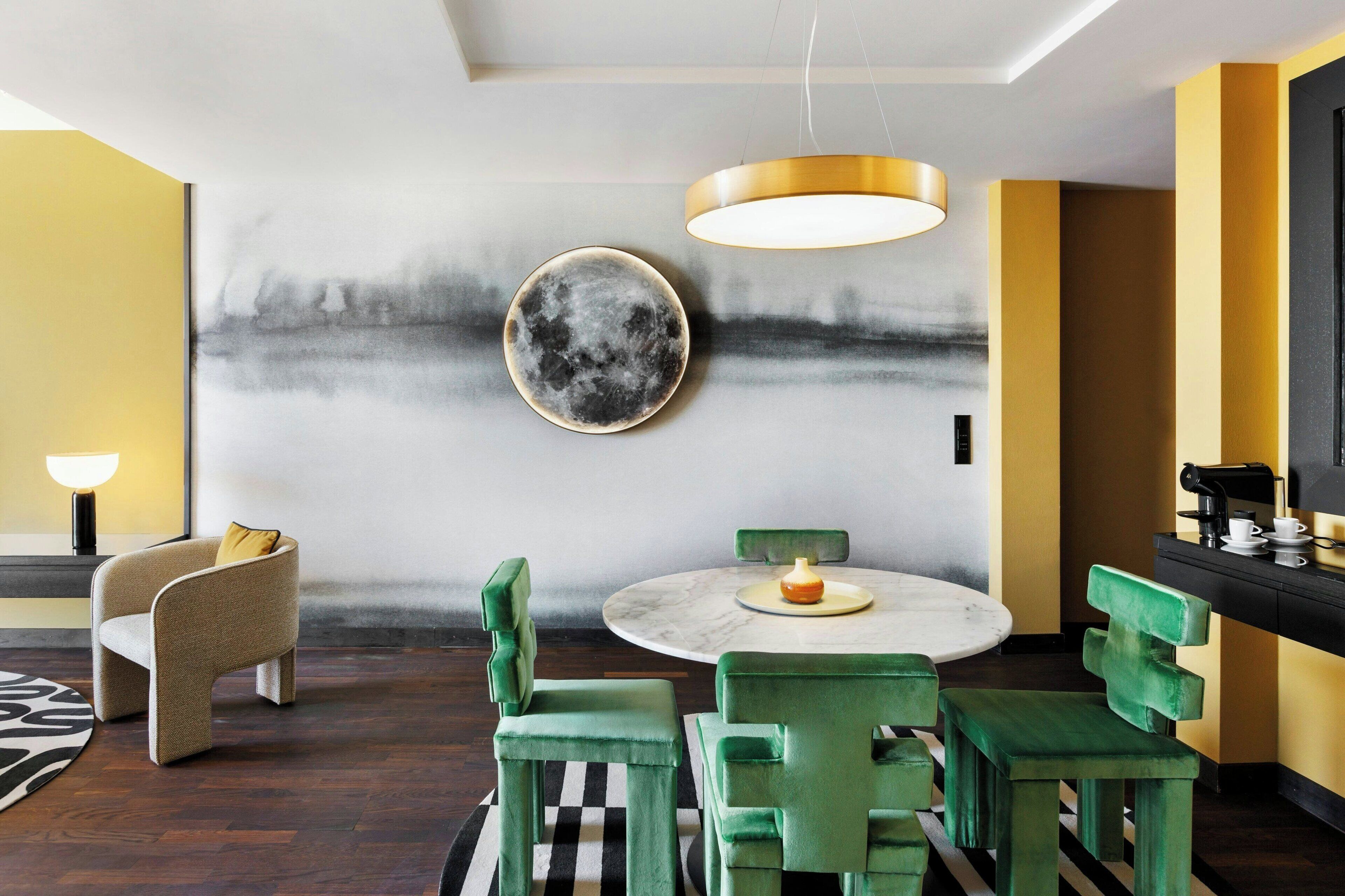Un comedor moderno con una mesa redonda, sillas tapizadas en verde y una obra de arte minimalista en la pared.