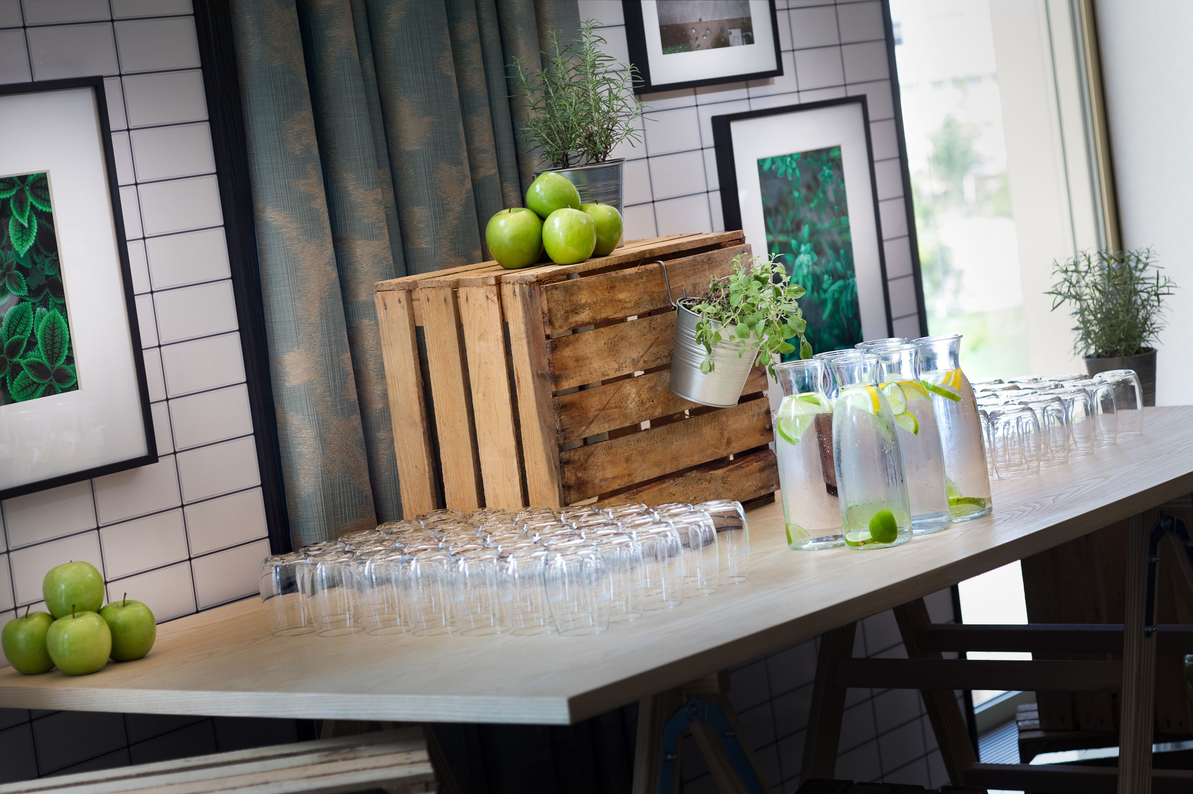 A table with green apples, a wooden crate, and clear glasses.