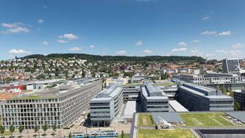 Eine moderne Stadtlandschaft mit einer Mischung aus Wohn- und Geschäftsgebäuden, einer Straßenbahnlinie und einem hügeligen Hintergrund.