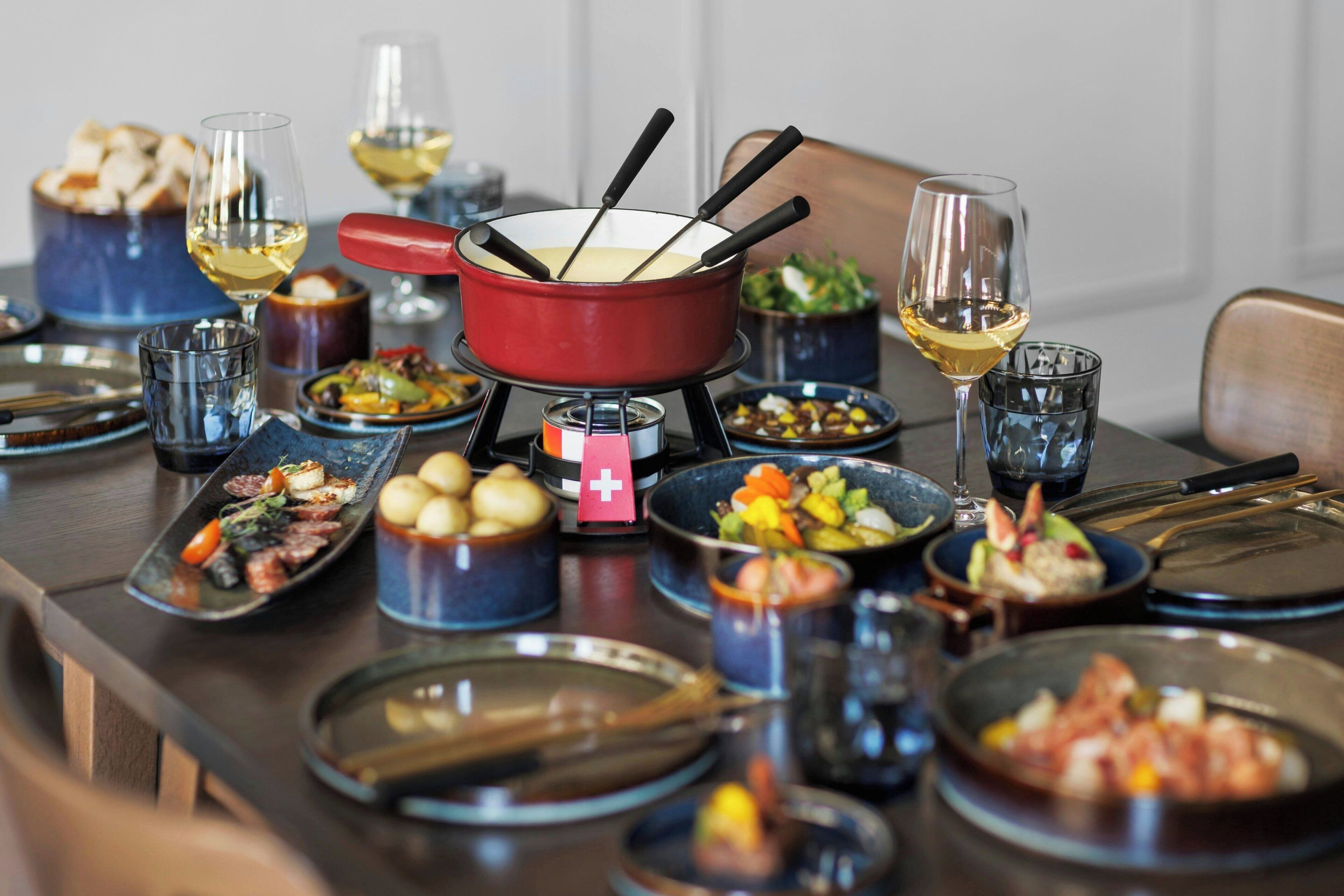 Ett matbord dukat med olika rätter, en fonduegryta och vinglas.