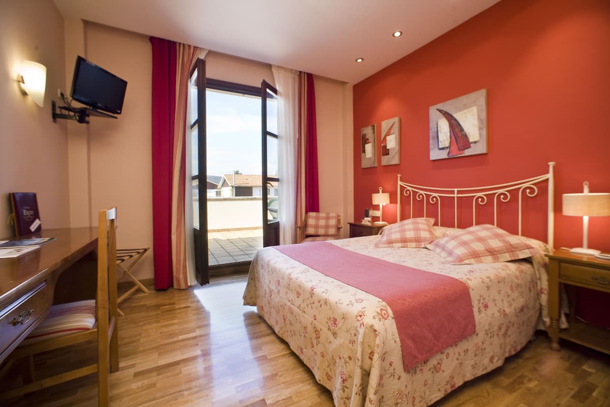 A hotel room with a bed, a desk, a chair, a TV, and a window with curtains.
