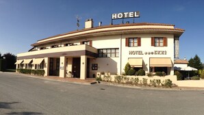 A hotel with a sign reading "HOTEL EKAÏ" and a bar sign. It features a curved facade with multiple windows and a flat roof.