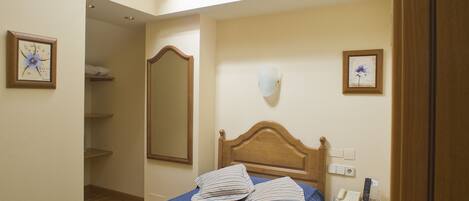 Een slaapkamer met dakraam, een bed met blauw beddegoed, een houten hoofdbord, een nachtkastje met lamp en een bijzettafeltje met telefoon.