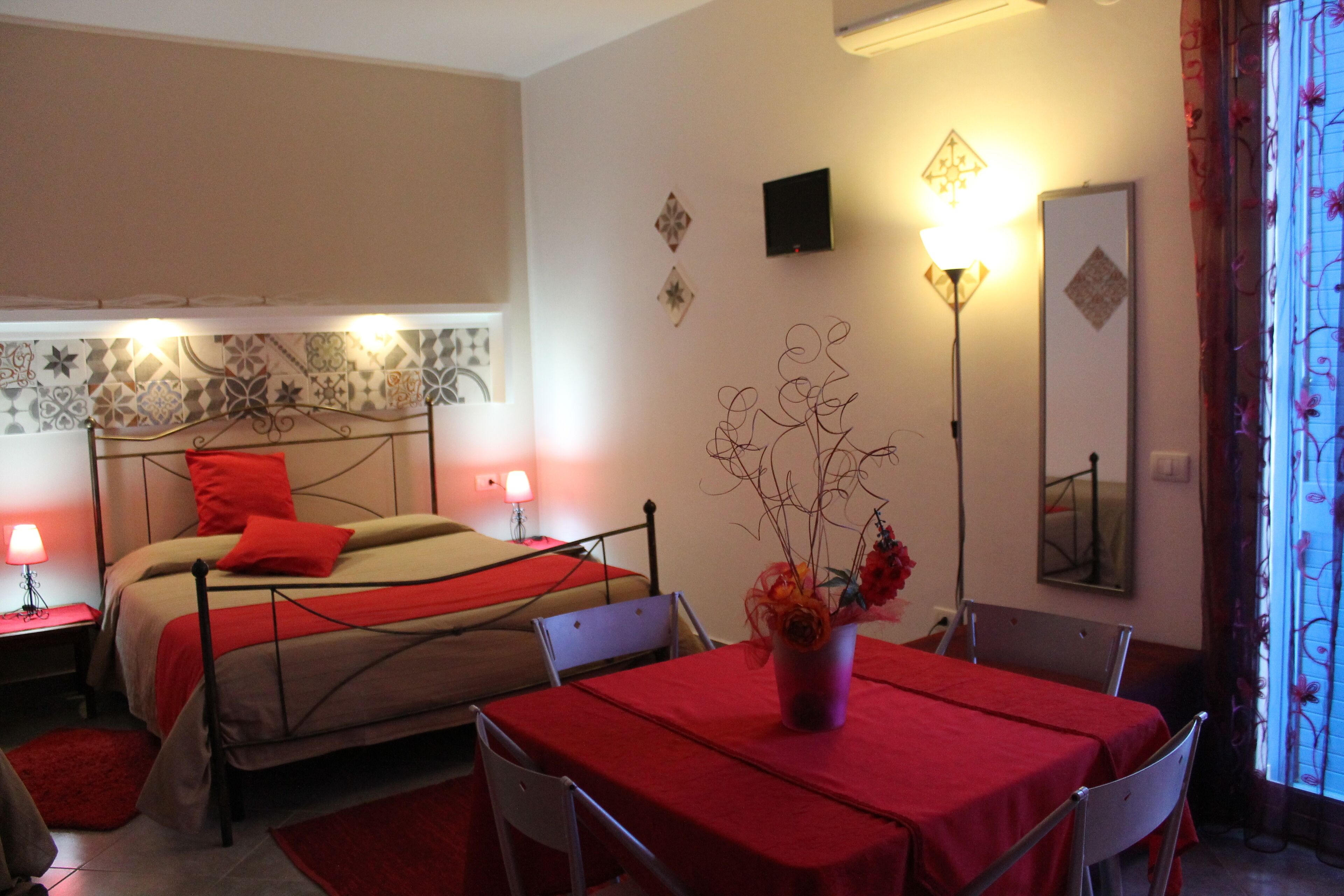 Une chambre d’hôtel avec deux lits, une table avec des chaises, un vase avec des fleurs, une lampe et un miroir.