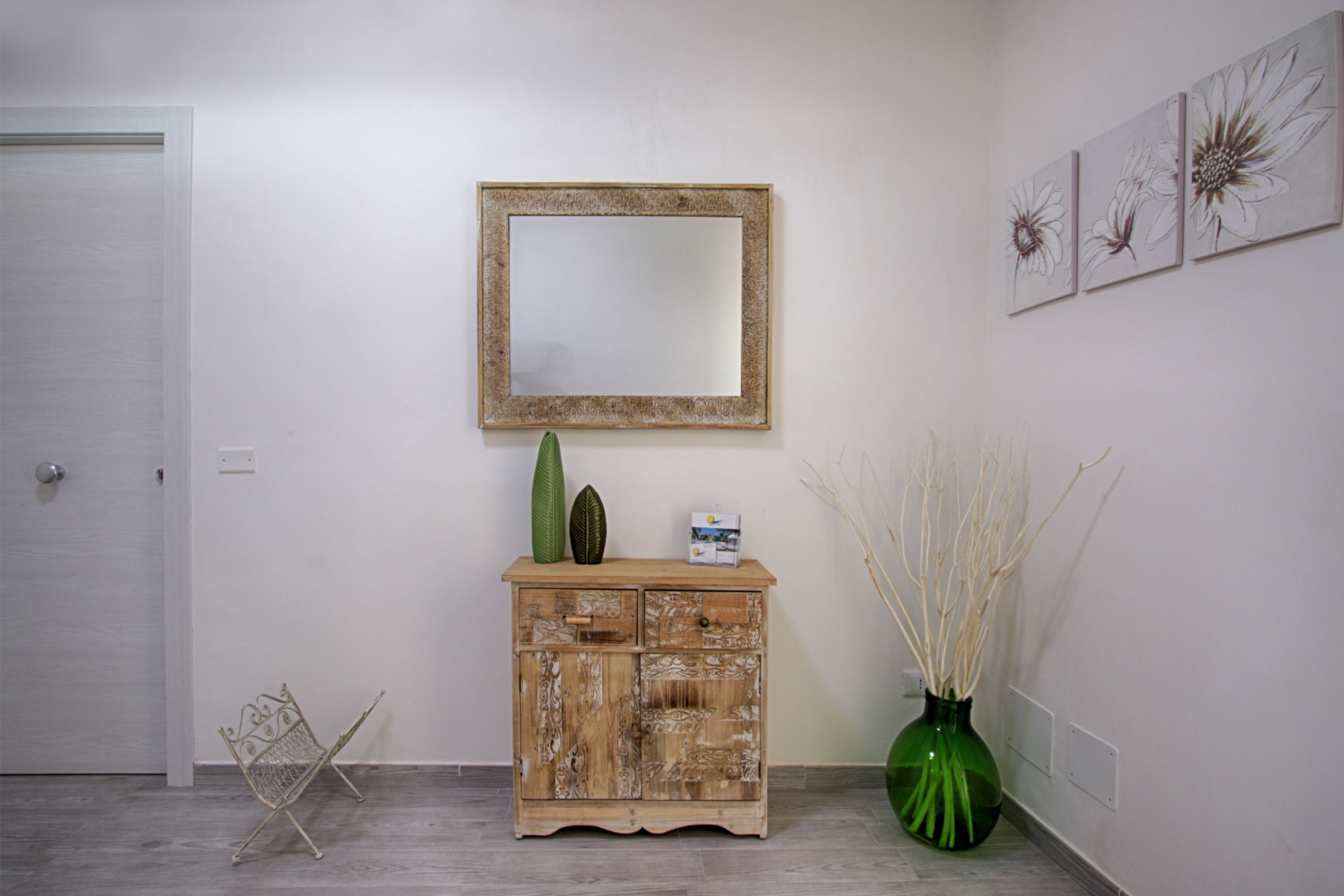 Un corridoio con un armadietto in legno, uno specchio e tre quadri floreali appesi al muro.