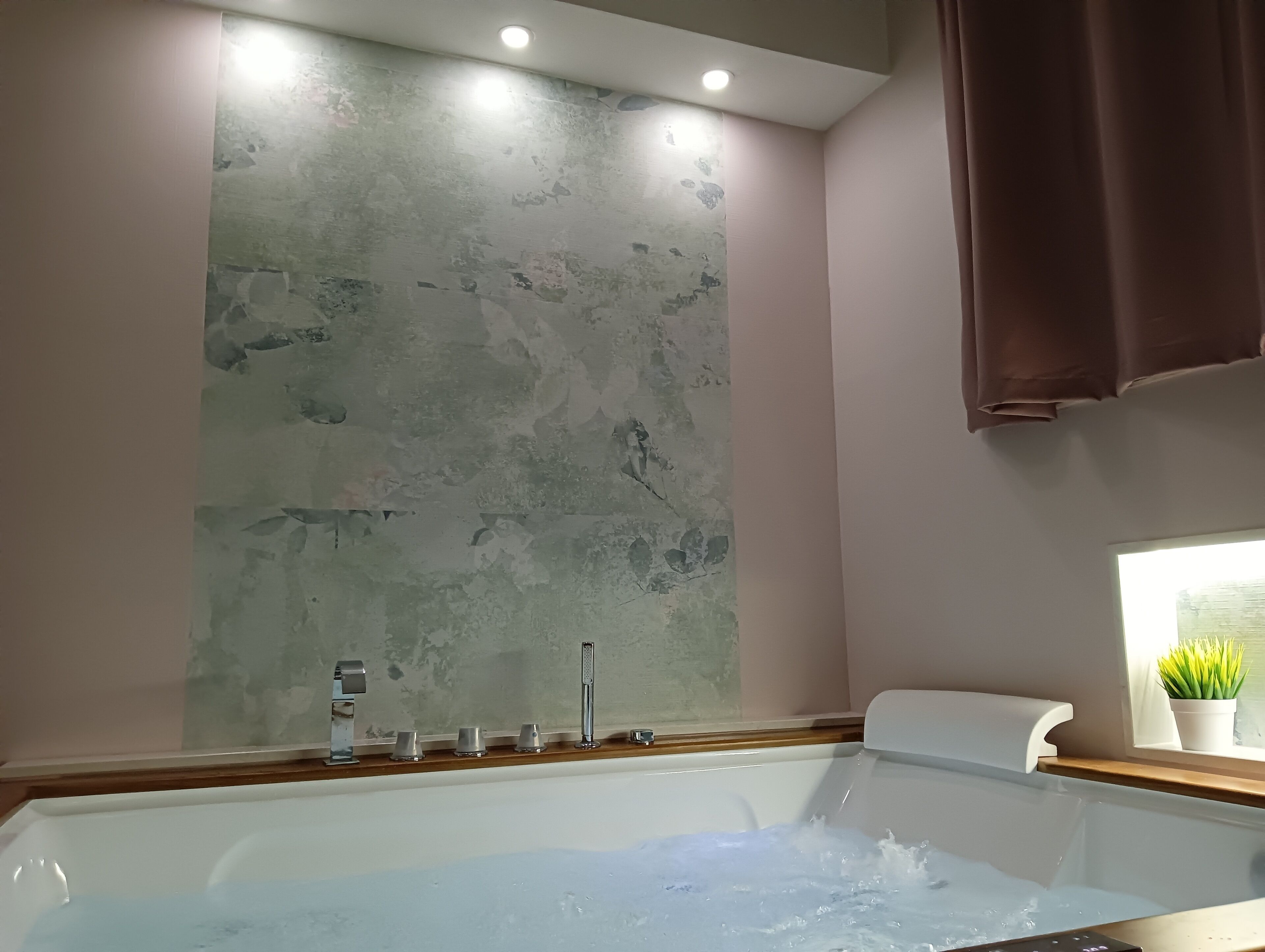 Une salle de bain avec une baignoire, une fenêtre agrémentée d’une plante et un mur à motifs.