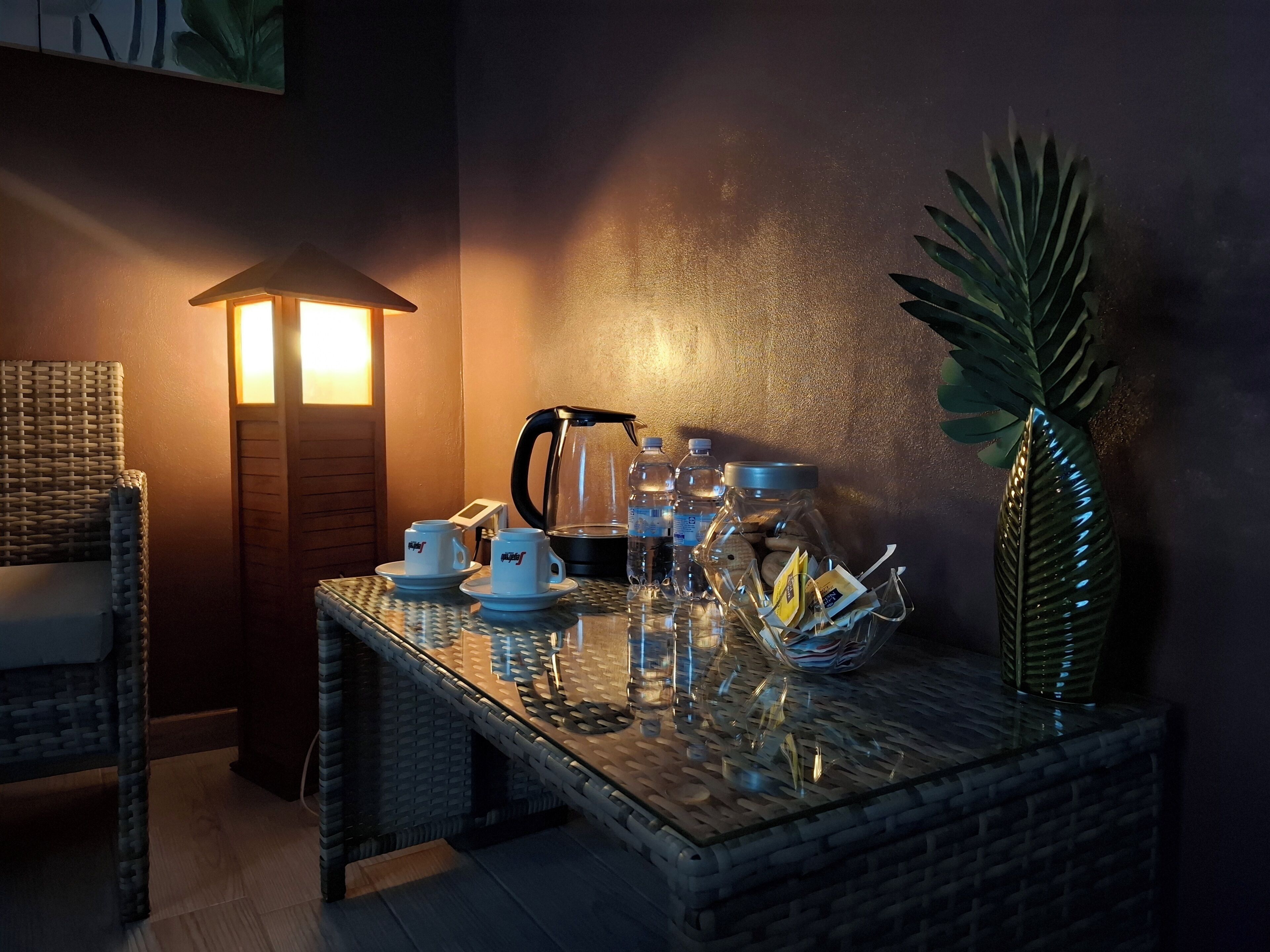 Una habitación acogedora con una silla de mimbre, una mesa con una cafetera, tazas y un tarro de vidrio con aperitivos.
