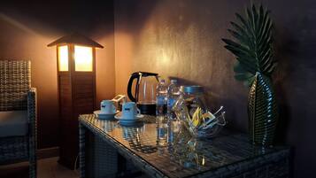 Una habitación acogedora con una silla de mimbre, una mesa con una cafetera, tazas y un tarro de vidrio con aperitivos.