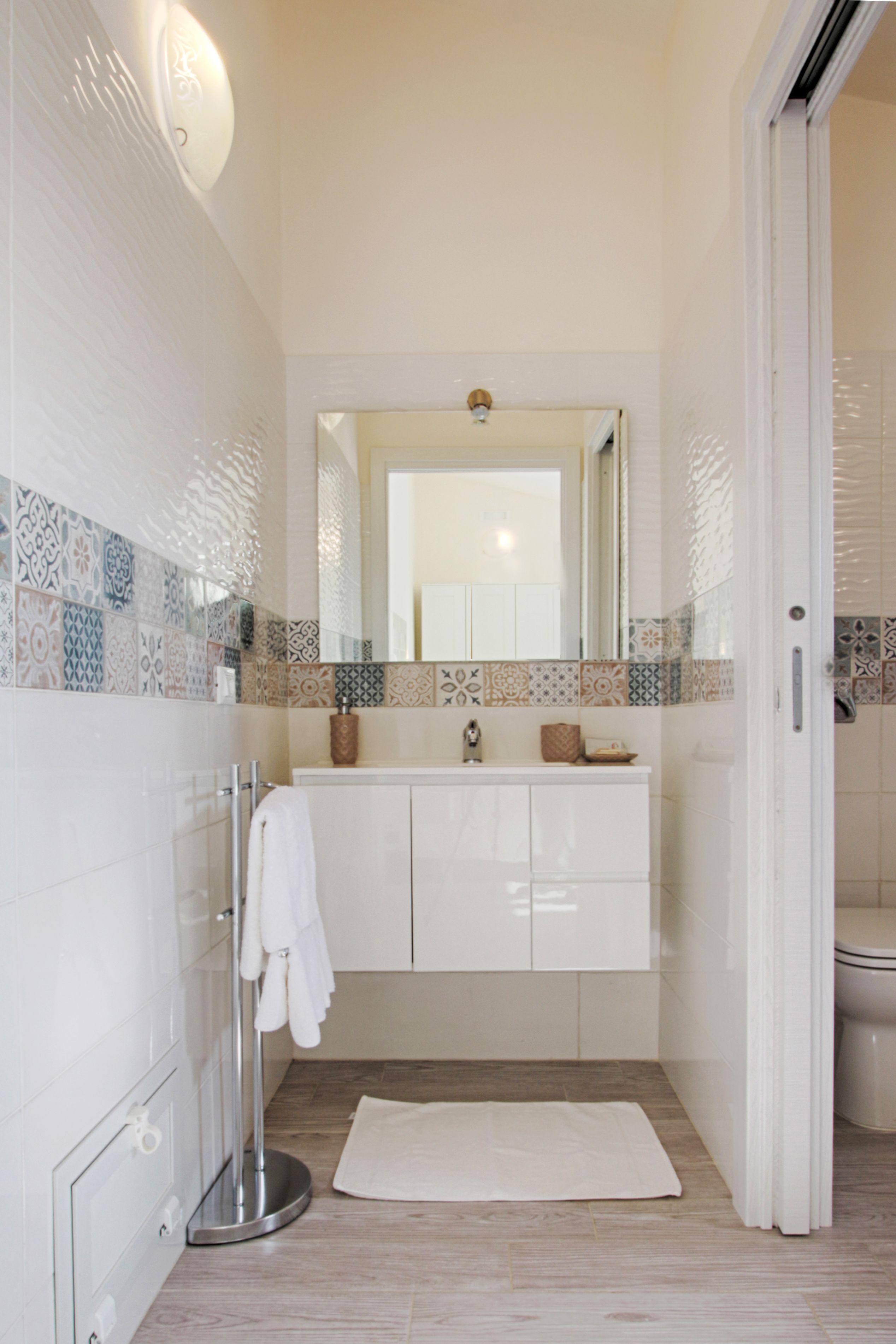 Un bagno con un mobile lavabo bianco, uno specchio e piastrelle decorate sulle pareti.