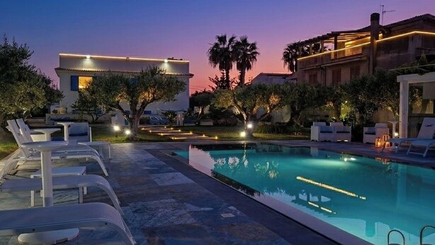 Zona junto a la piscina con sillas de descanso, una piscina y un cielo al atardecer.