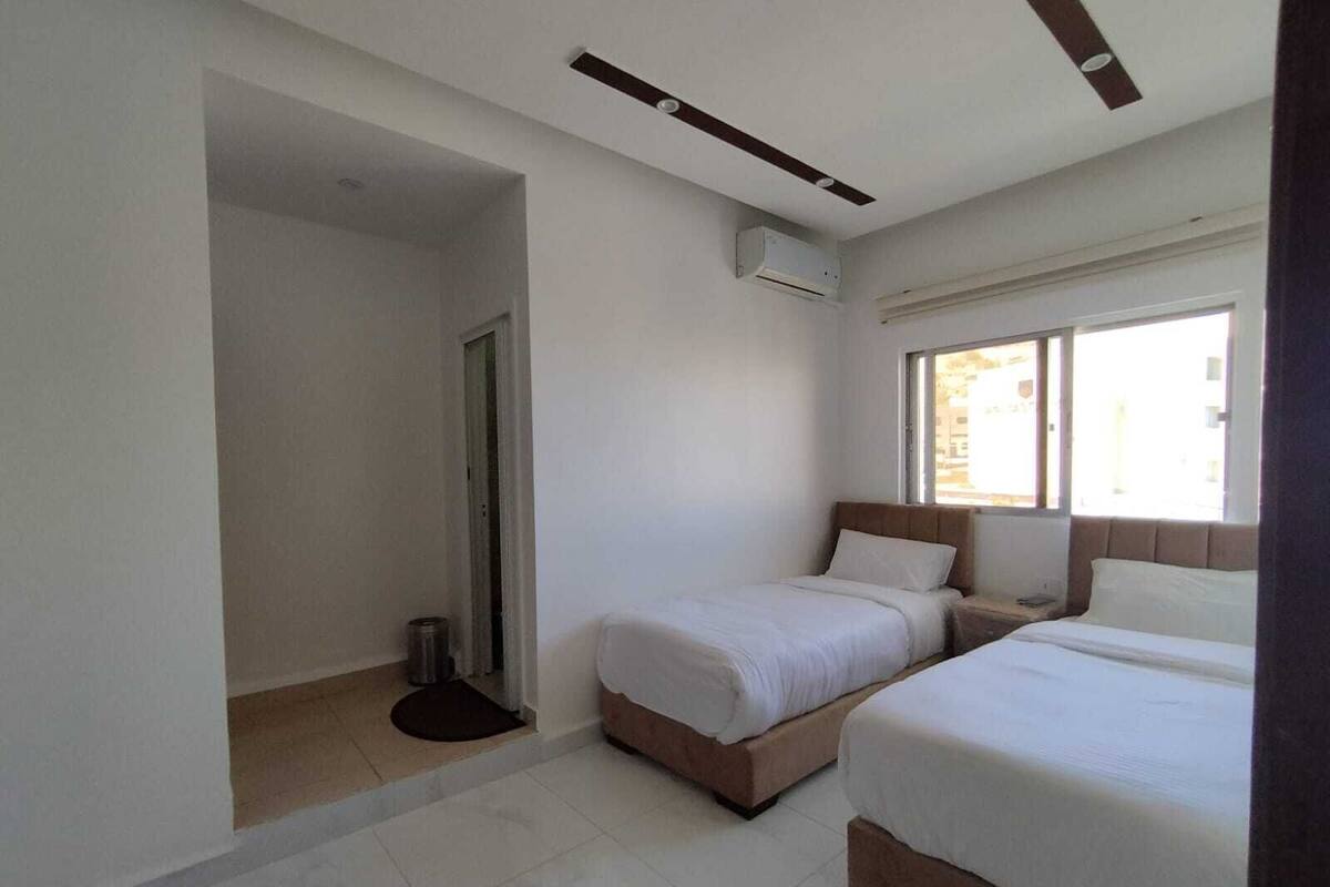 A hotel room with two beds, a window, an air conditioning unit, and a door leading to a bathroom.