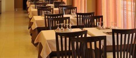 Un restaurante con varias mesas y sillas, cada conjunto con copas de vino y cubiertos.