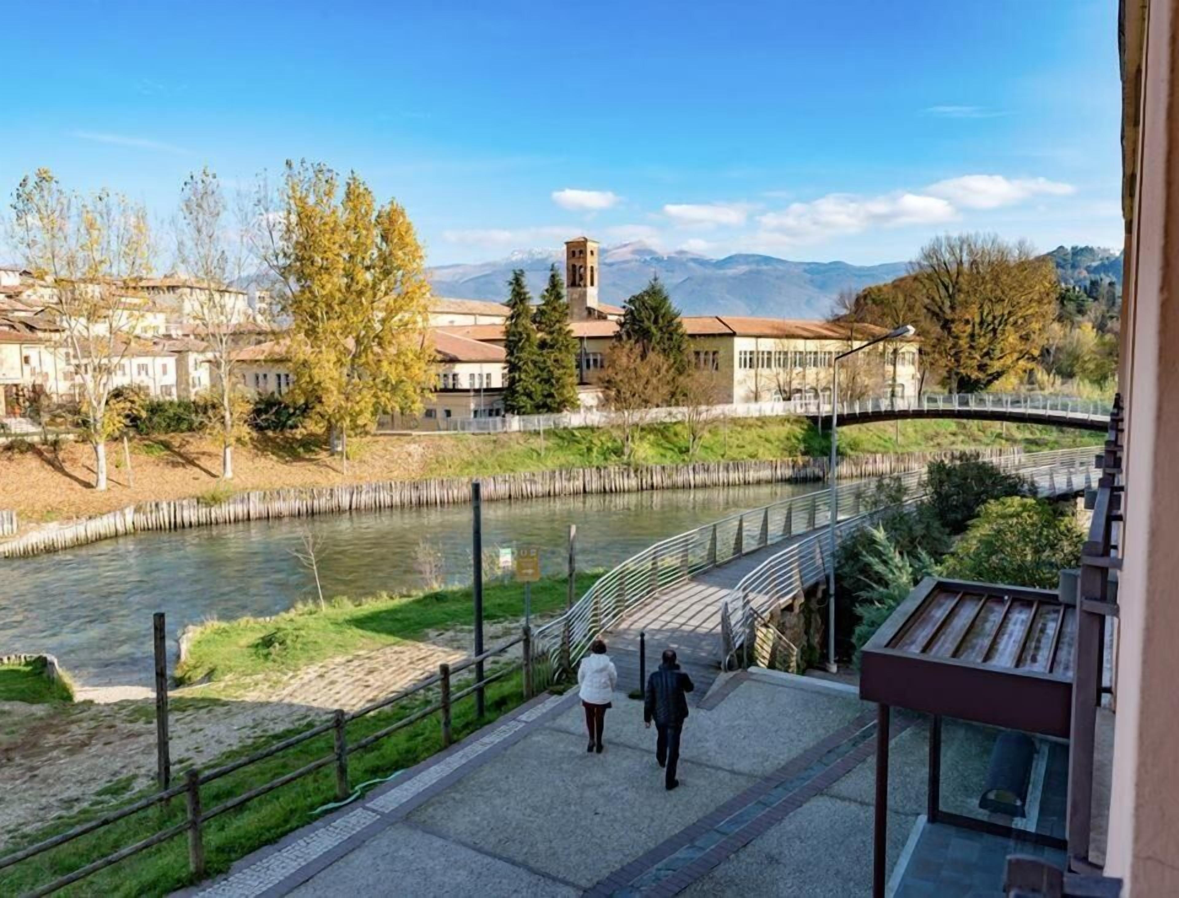 A riverside walkway with a bridge, buildings, and mountains in the background.