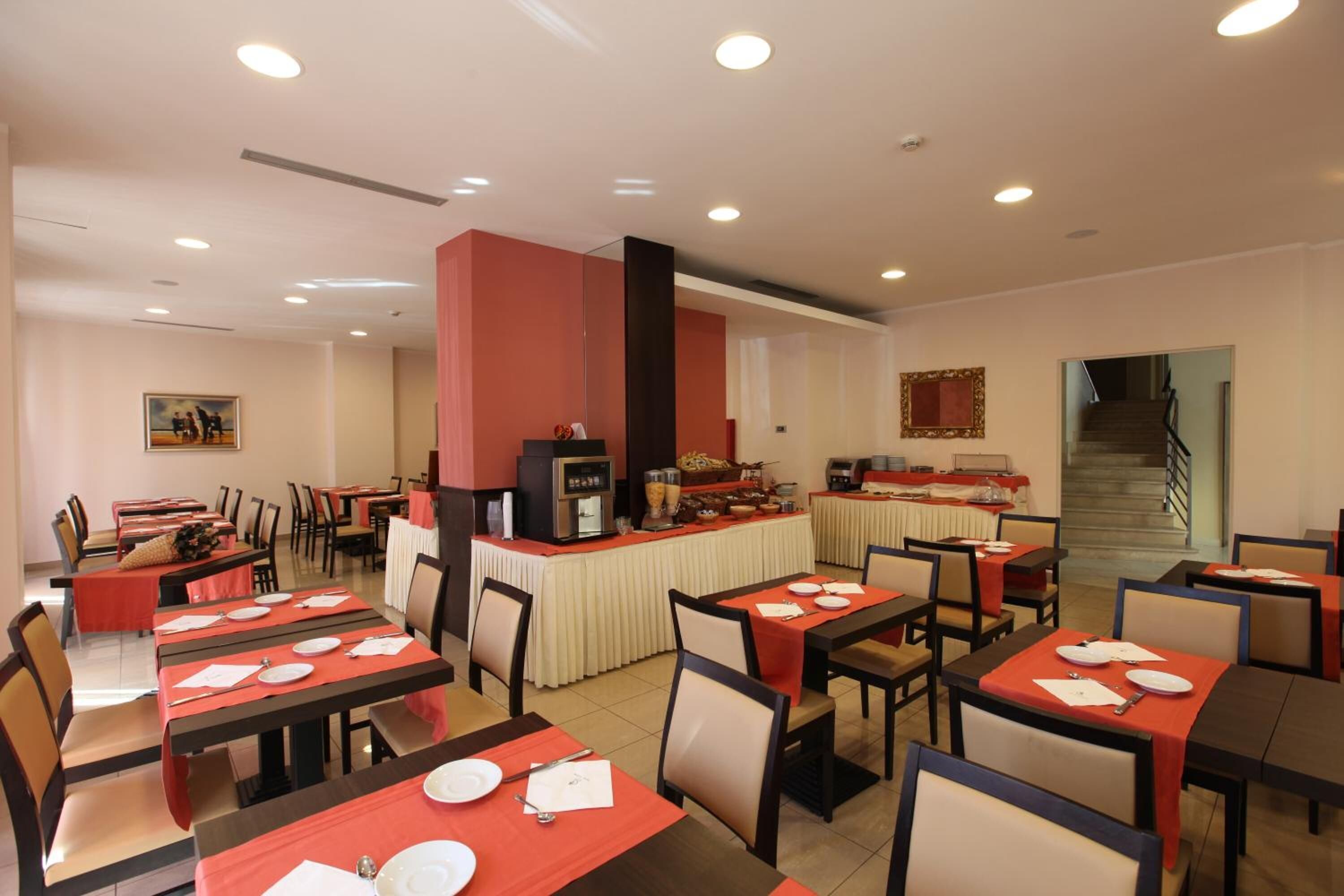 Ein Speisesaal eines Hotels mit mehreren Tischen und Stühlen, einer Buffettheke und einer Treppe zu einer oberen Etage.