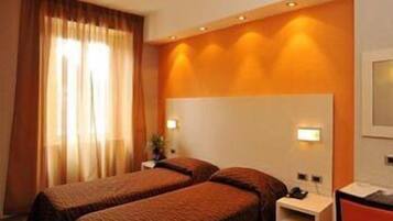 Ein Hotelzimmer mit zwei Einzelbetten, einem Nachttisch, einem Schreibtisch und einem Fenster mit Vorhängen.