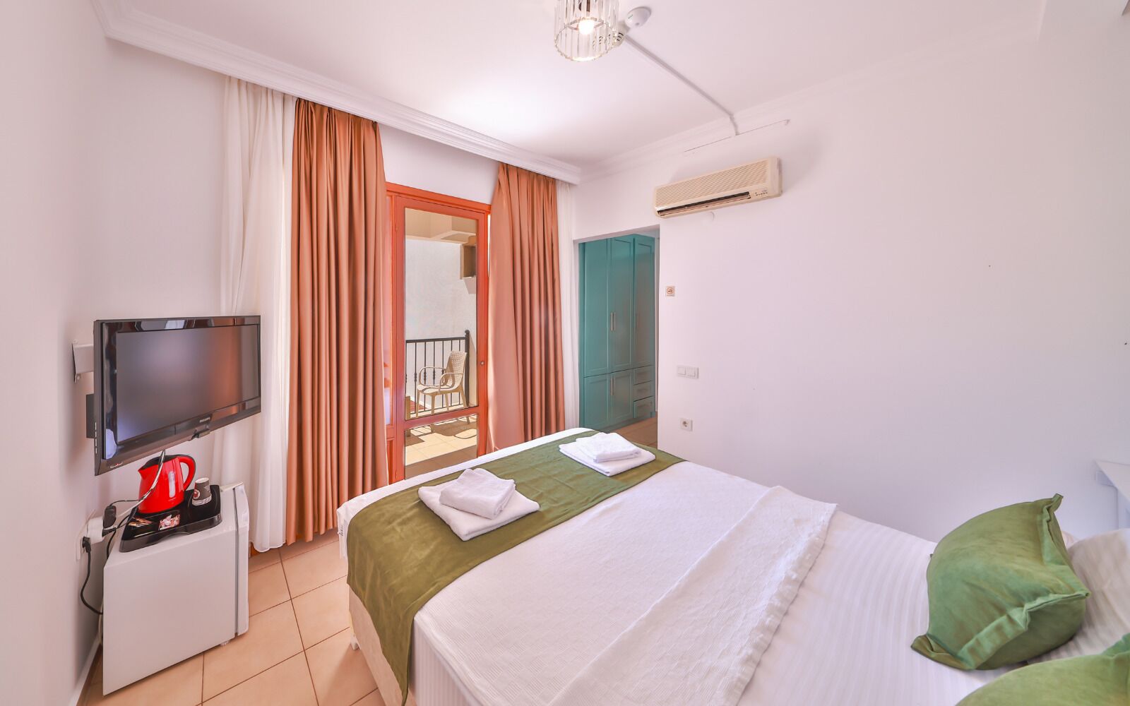 Una habitación de hotel con cama, televisor, cafetera, puerta corrediza a un balcón y unidad de aire acondicionado.