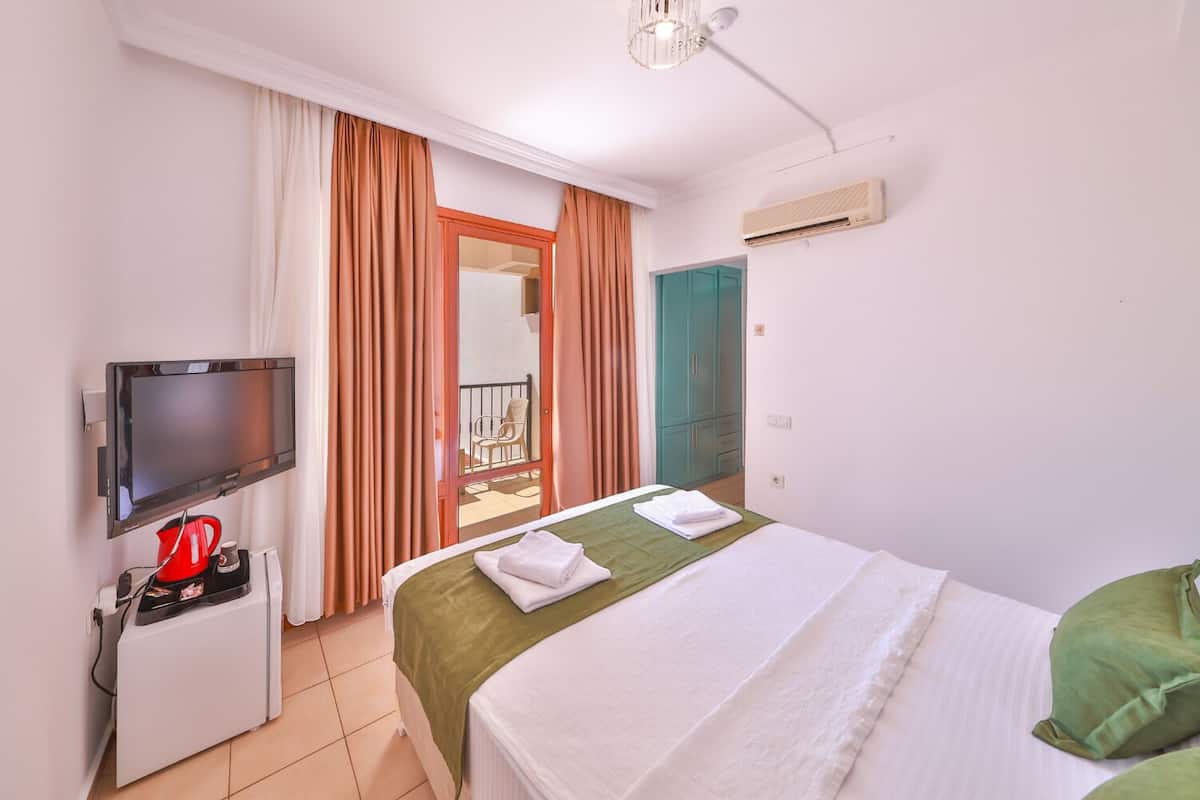 A hotel room with a bed, a TV, a coffee maker, a sliding door to a balcony, and an air conditioning unit.