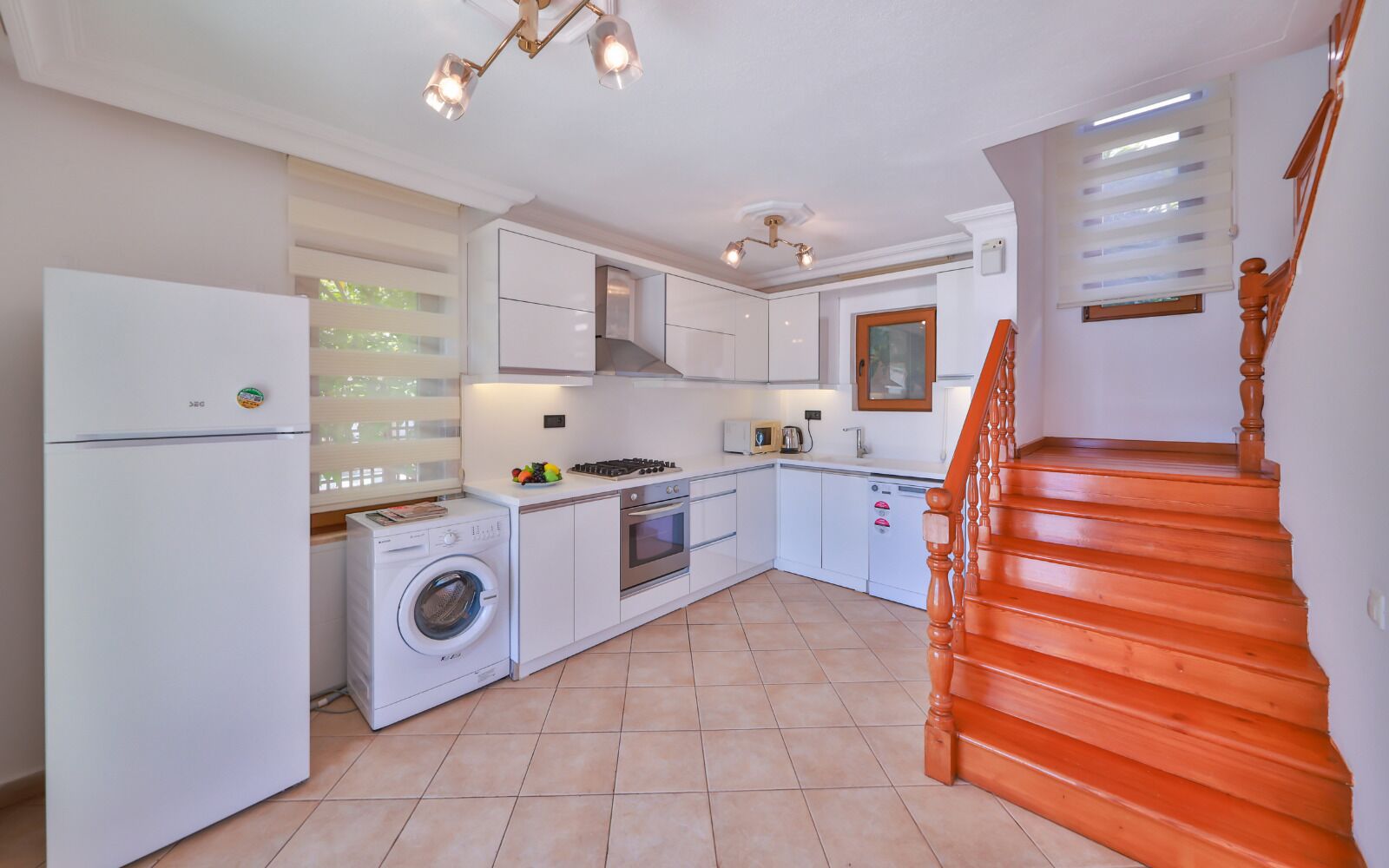 A compact kitchen with a washing machine, oven, and a wooden staircase.