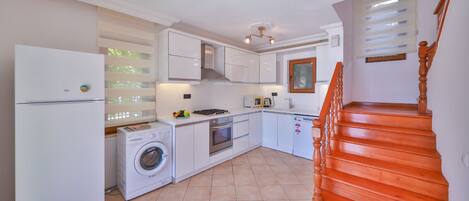 A compact kitchen with a washing machine, oven, and a wooden staircase.