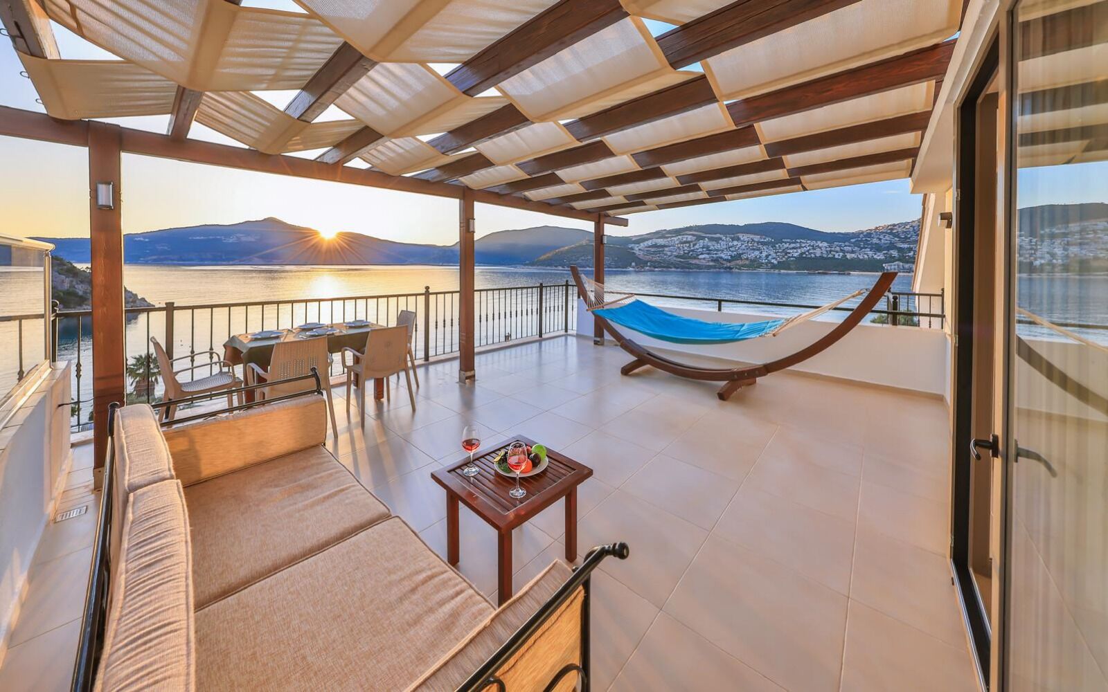 A balcony with a hammock, seating, and a table with a glass of wine.