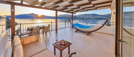 A balcony with a hammock, seating, and a table with a glass of wine.