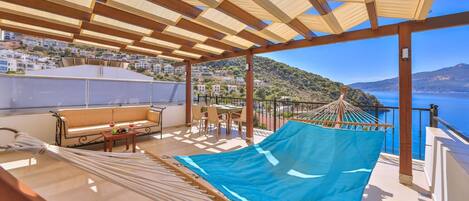 A balcony with a hammock, a sofa, and a table with a drink.