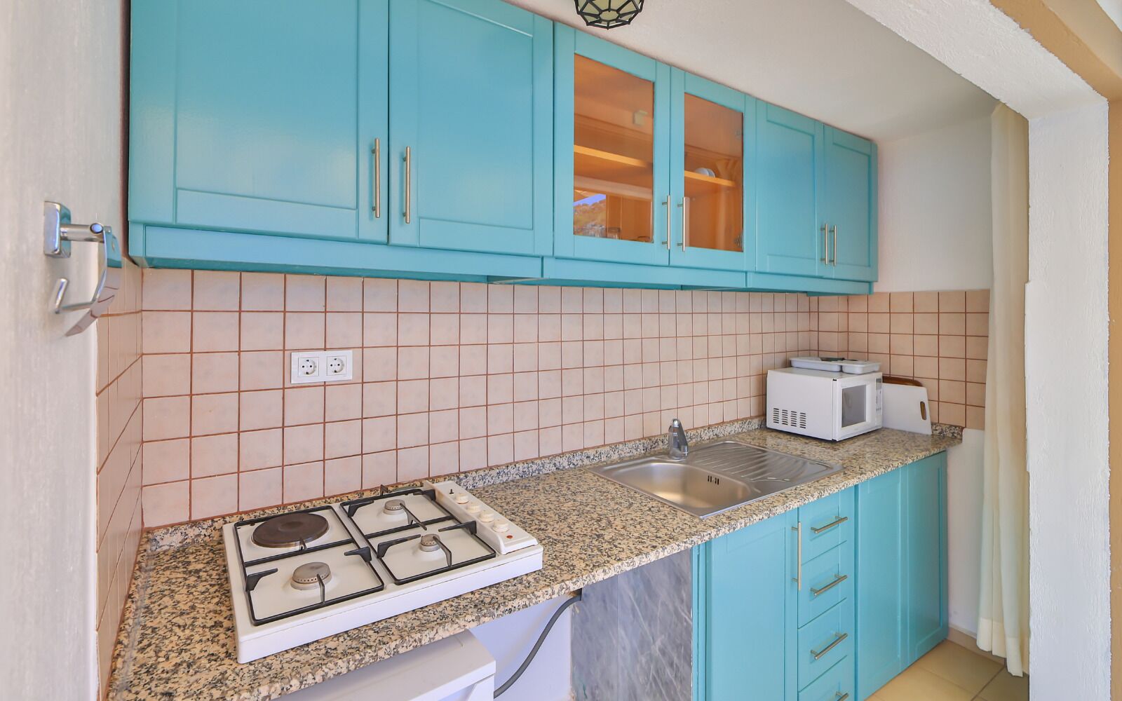 Una cocina con armarios azul verdoso, encimera de granito, estufa, fregadero y microondas.