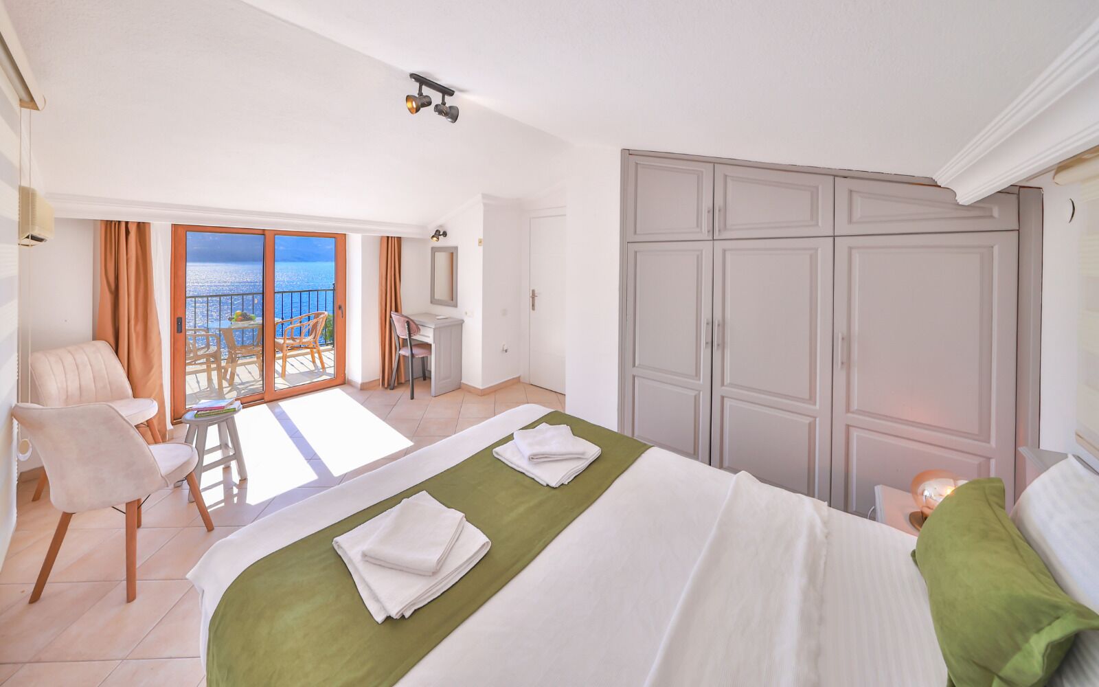 A hotel room with a bed, a desk, a chair, a wardrobe, and a balcony with a view.