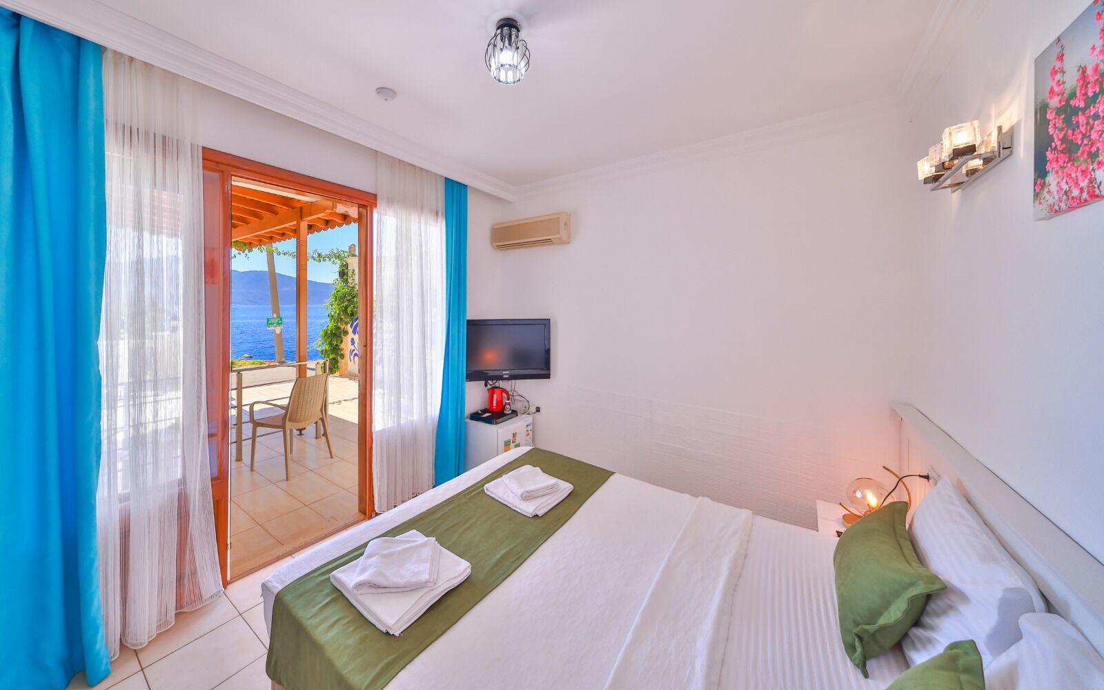 Habitación de hotel con cama, televisión, escritorio con tetera y vista al mar.