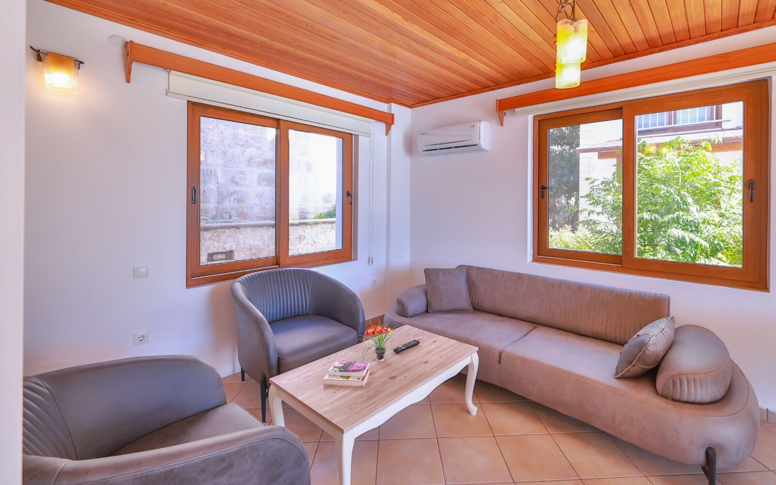A living room with a sofa, two armchairs, a coffee table, and large windows with wooden frames.