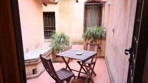 Un patio con una mesa y sillas, plantas en macetas y un edificio con contraventanas.